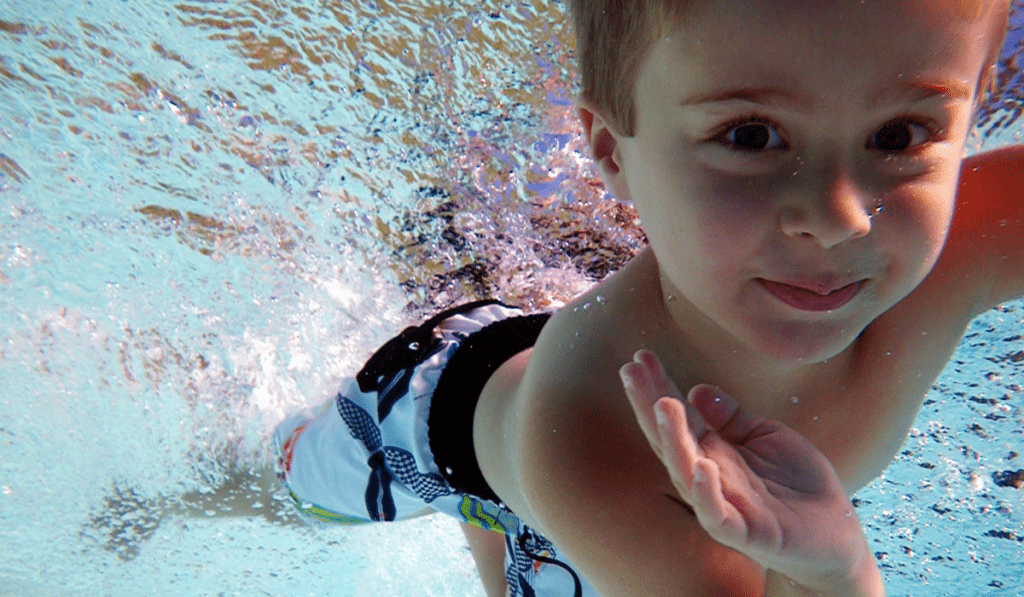 boy swimming underwater and waving high