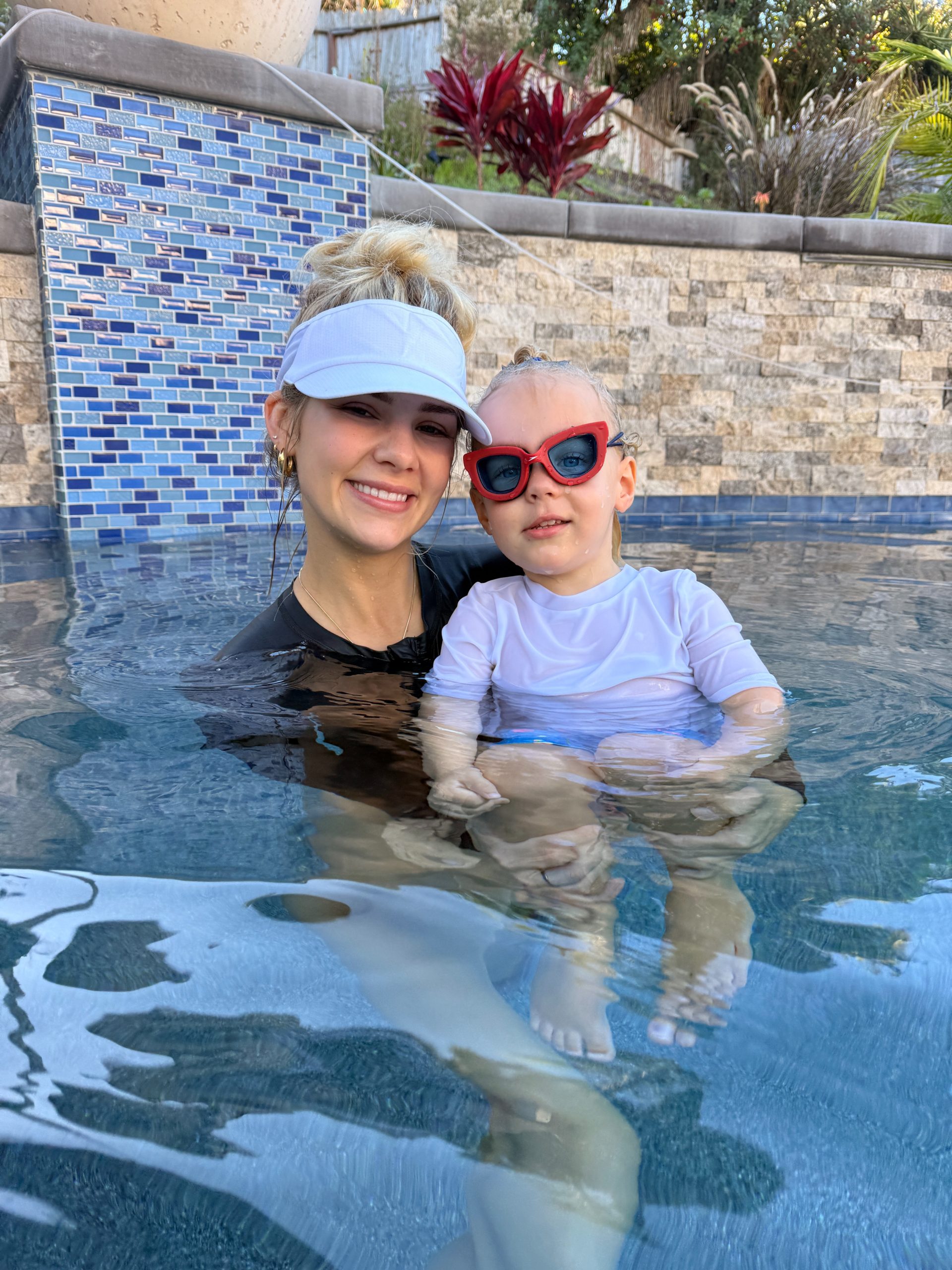 Miss Emma with a student wearing red goggles in the pool.