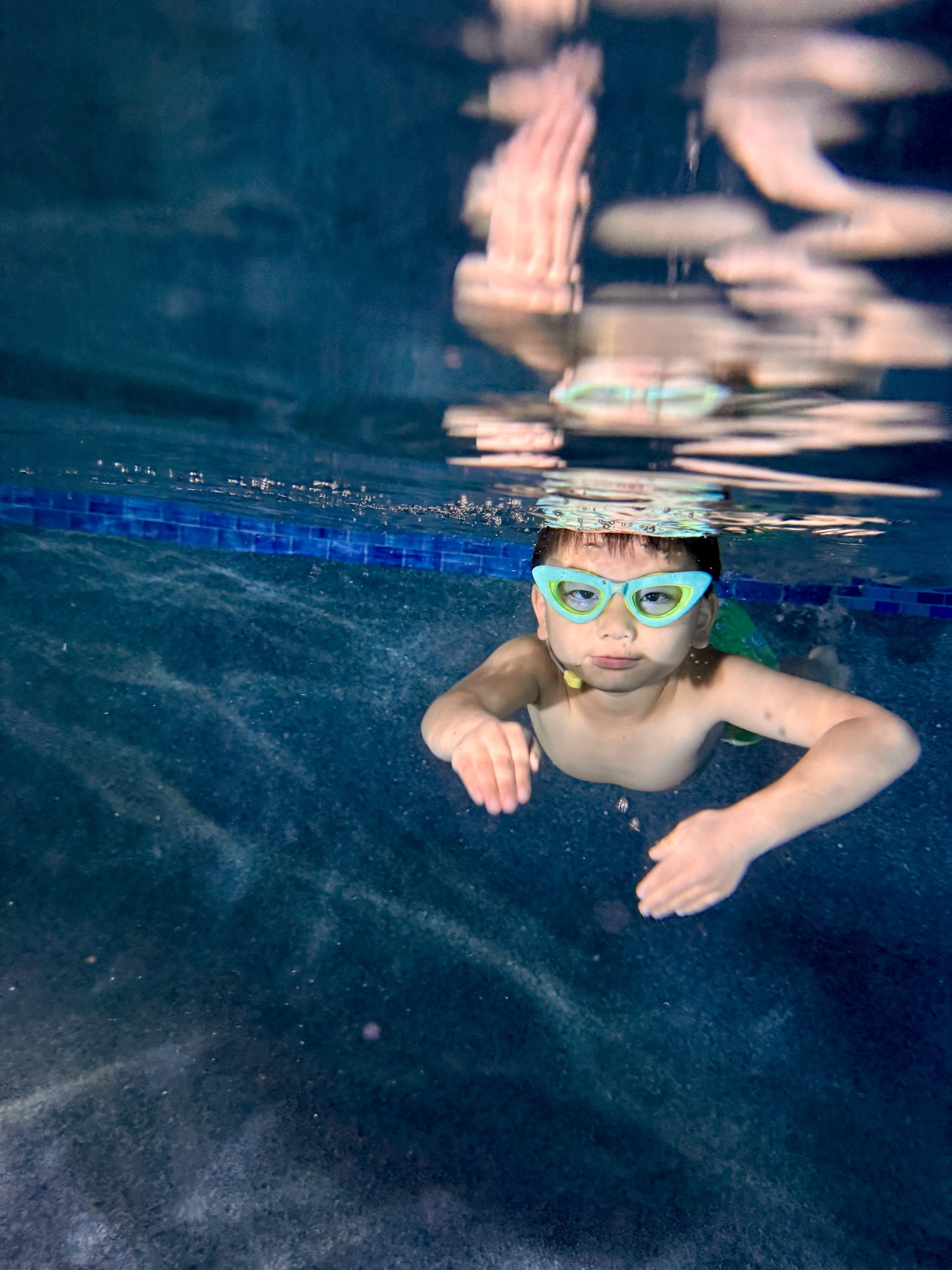 Swimmer wearing goggles in an illuminated pool.